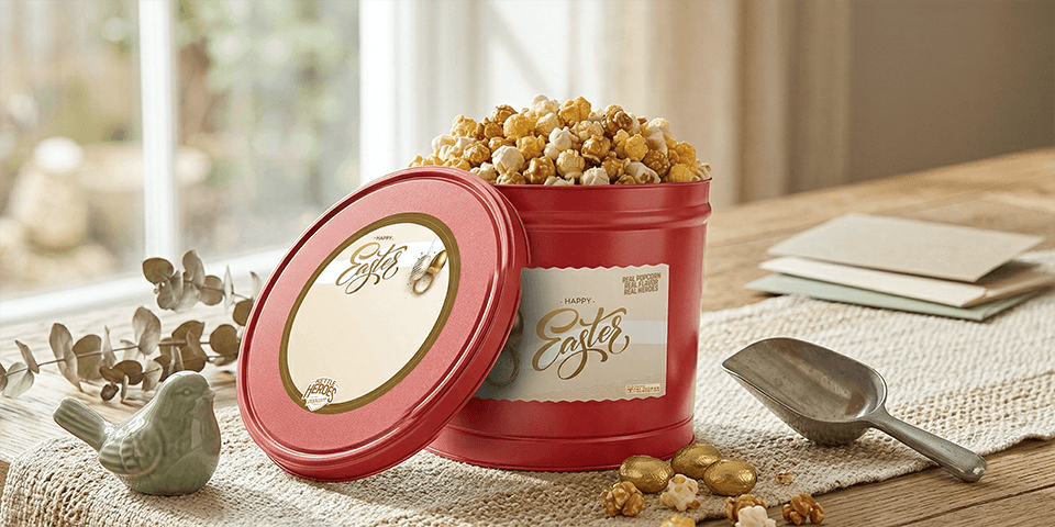 Kettle Heroes red Easter popcorn gift tin filled with fresh gourmet popcorn on a wooden table surrounded by decorated Easter eggs and spring branches